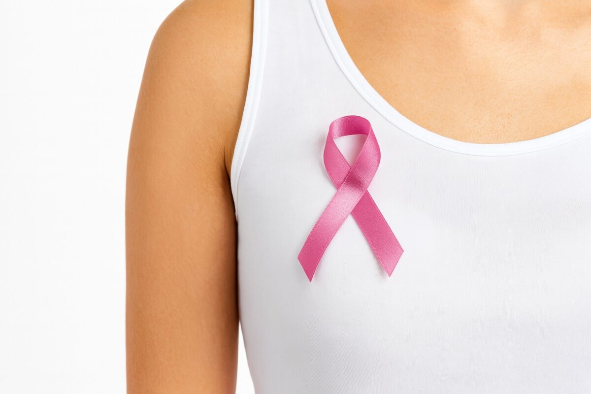 Close-up of a pink breast cancer awareness ribbon pinned to a woman's white tank top, symbolizing women's health support and prevention. Close-up of a pink breast cancer awareness ribbon pinned to a woman's white tank top, symbolizing women's health support and prevention.